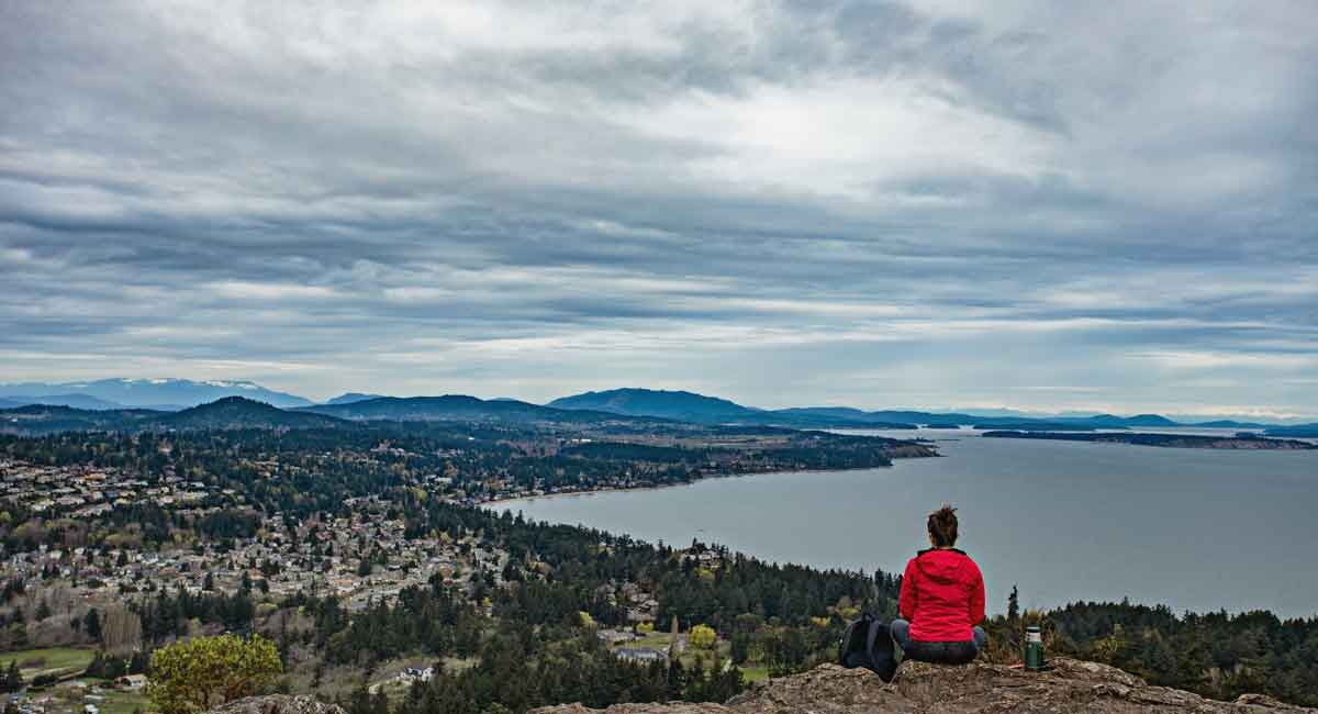 A man is sitting at the top of a mountain and looks at the ocean.